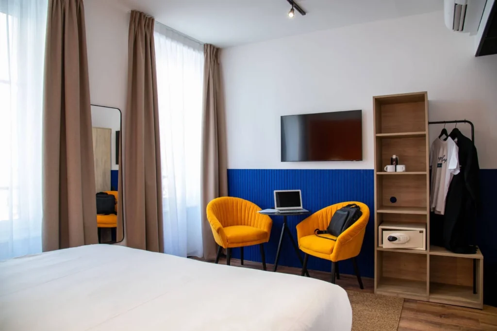 Chambre Double Supérieure du ClapClap Hôtel Strasbourg avec lit, fauteuils jaunes, mur bleu, TV murale et étagère bois