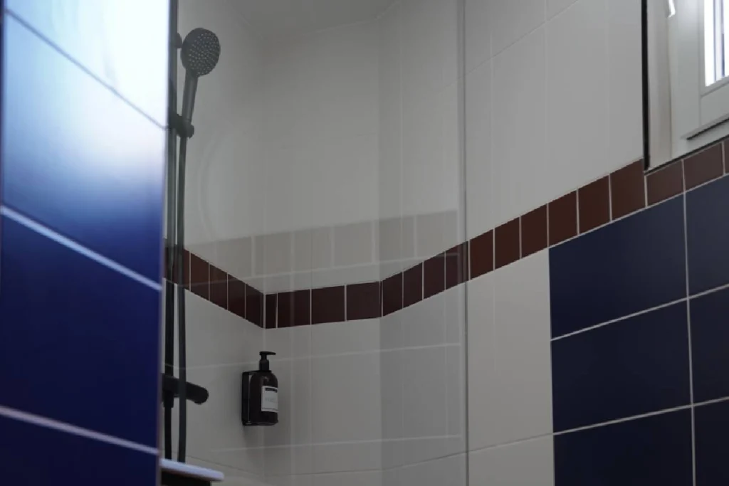 Douche du ClapClap Hôtel Strasbourg avec carrelage bleu cobalt, frise bordeaux et colonne de douche noire