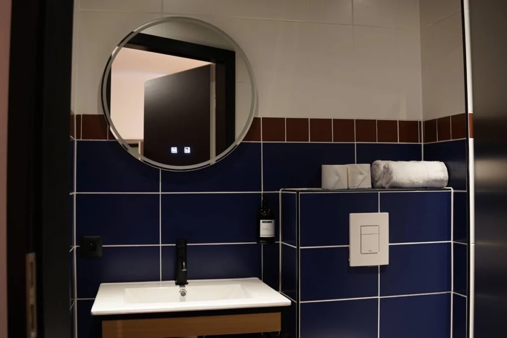 Salle de bain du ClapClap Hôtel Strasbourg avec vasque, robinetterie noire, miroir rond, carrelage bleu cobalt et frise bordeaux