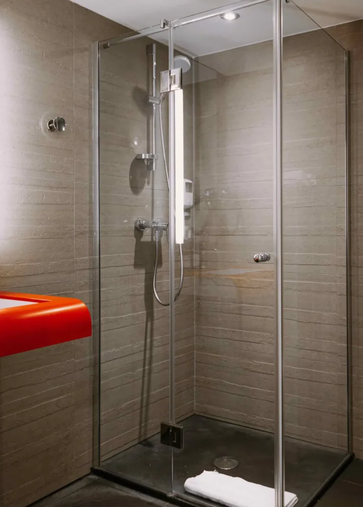 Douche à l'italienne vitrée de la chambre Famille 6 du ClapClap Hôtel Strasbourg avec carrelage taupe et tablette rouge