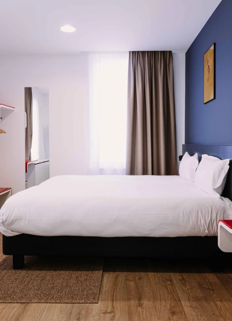 Lit double de la chambre Famille 6 personnes du ClapClap Hôtel Strasbourg avec mur bleu, rideaux taupe et parquet