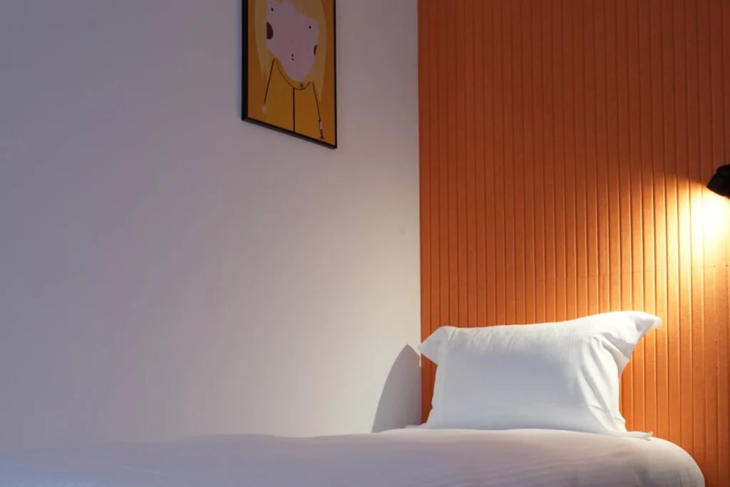 Chambre Solo du ClapClap Hôtel Strasbourg avec lit, mur orange, applique et affiche