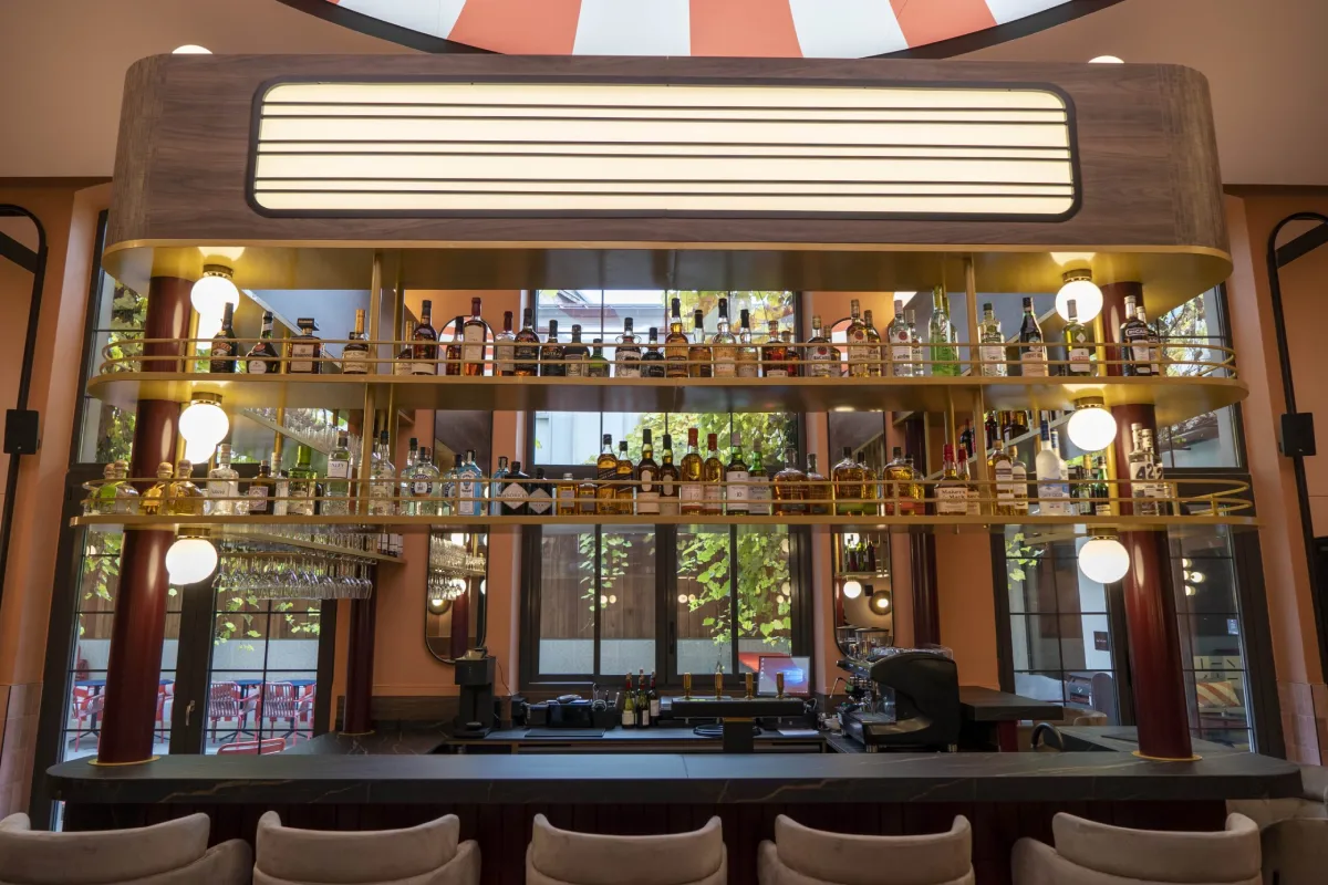 Vue frontale du bar du Clap Show Strasbourg avec étagères de bouteilles, éclairage vintage et plafond rayé rouge et blanc