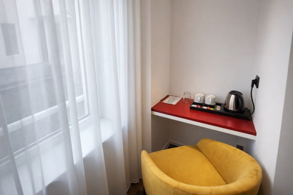 Coin bureau avec plateau rouge, bouilloire, tasses et fauteuil jaune près d'une fenêtre lumineuse