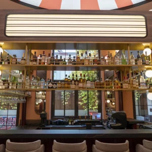 Vue frontale du bar du Clap Show Strasbourg avec étagères de bouteilles, éclairage vintage et plafond rayé rouge et blanc