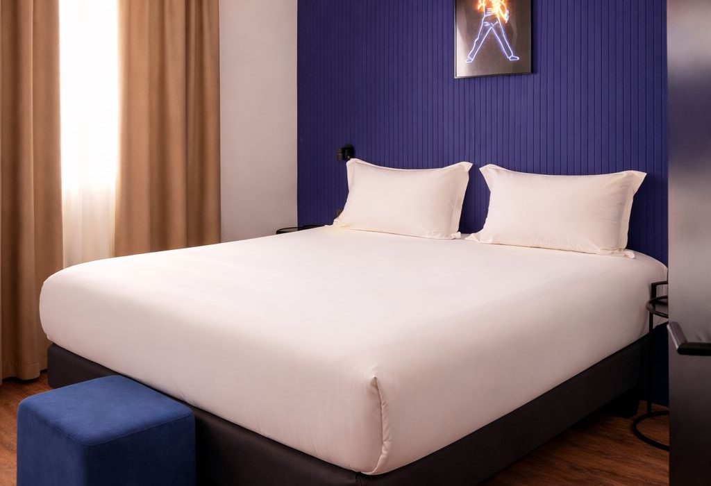 Chambre avec grand lit, tête de lit bleu nuit, tabouret velours bleu et affiche néon, ClapClap Hotel Strasbourg