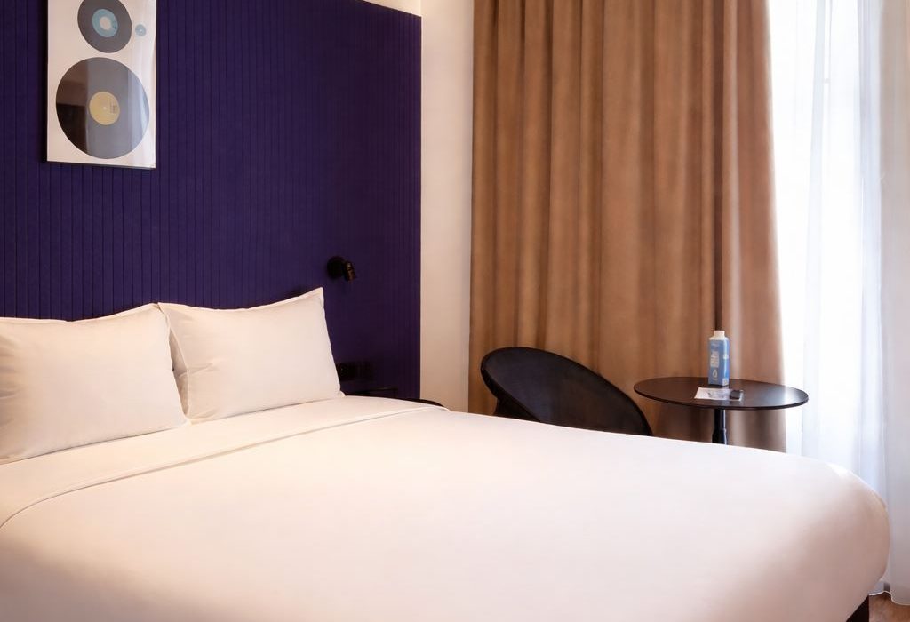 Chambre avec lit double, tête de lit violet foncé, parquet en bois et rideaux beiges, ClapClap Hotel Strasbourg