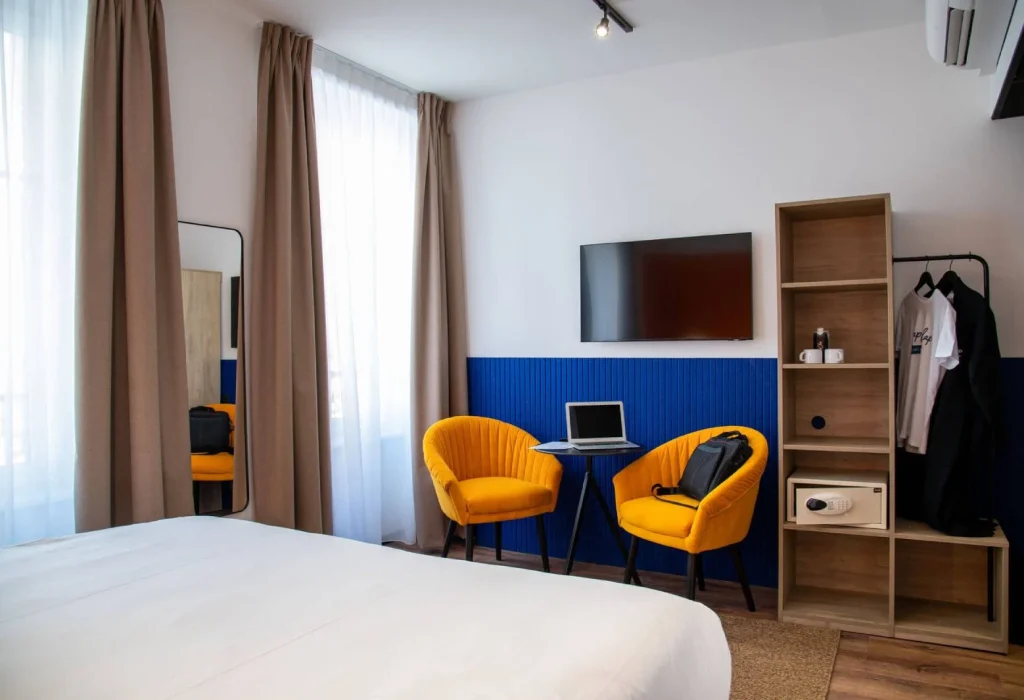 Chambre Double Supérieure du ClapClap Hôtel Strasbourg avec lit, fauteuils jaunes, mur bleu, TV murale et étagère bois