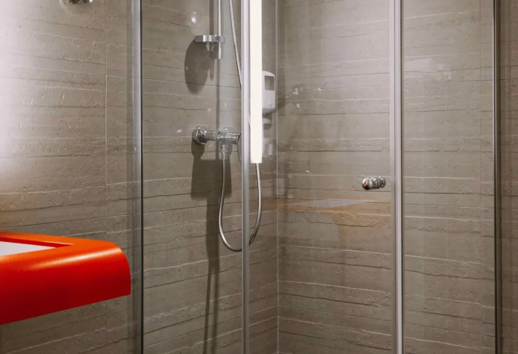 Douche à l'italienne vitrée de la chambre Famille 6 du ClapClap Hôtel Strasbourg avec carrelage taupe et tablette rouge