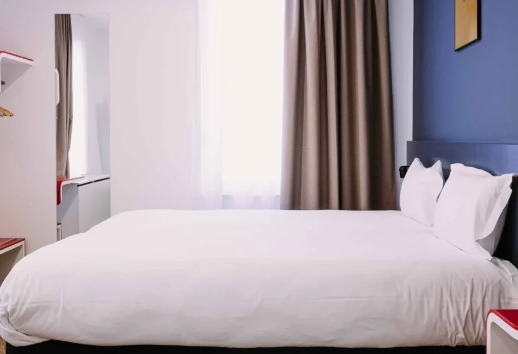 Lit double de la chambre Famille 6 personnes du ClapClap Hôtel Strasbourg avec mur bleu, rideaux taupe et parquet
