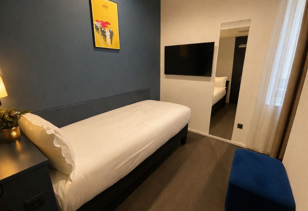 Chambre simple avec lit une place, tête de lit gris ardoise, affiche Cannes et pouf bleu marine