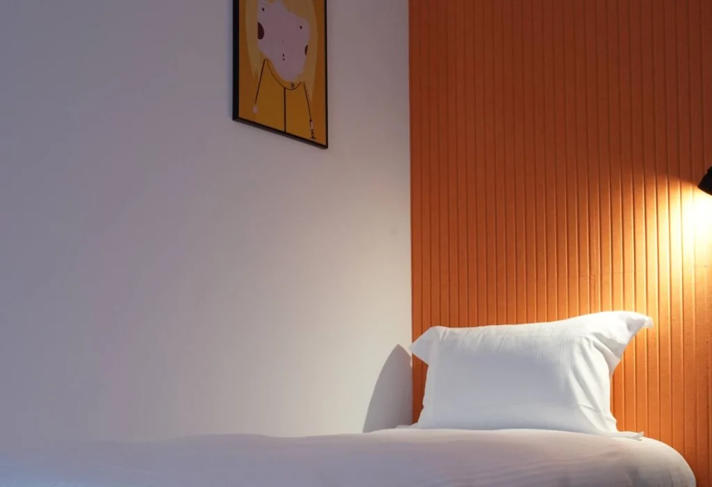 Chambre Solo du ClapClap Hôtel Strasbourg avec lit, mur orange, applique et affiche