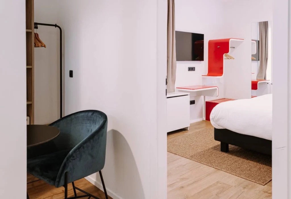 Chambre Tribu du ClapClap Hôtel Strasbourg avec espace bureau fauteuil vert, lit double, mobilier rouge design et TV murale
