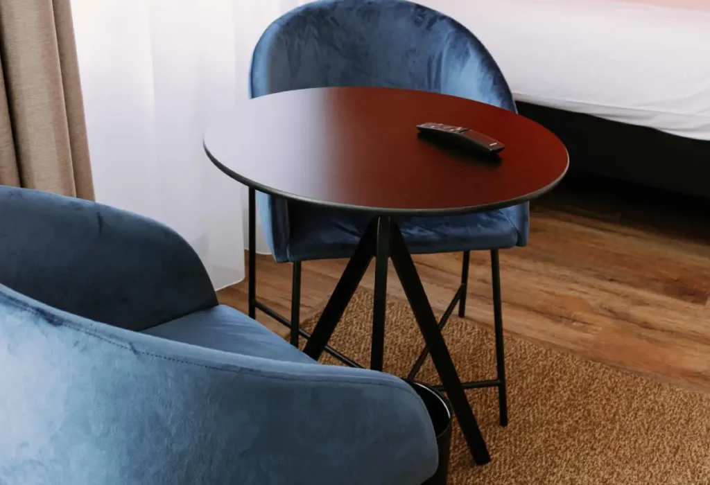 Détail chambre Triple du ClapClap Hôtel Strasbourg : chaises velours bleu, table ronde et lit avec mur orange en arrière-plan