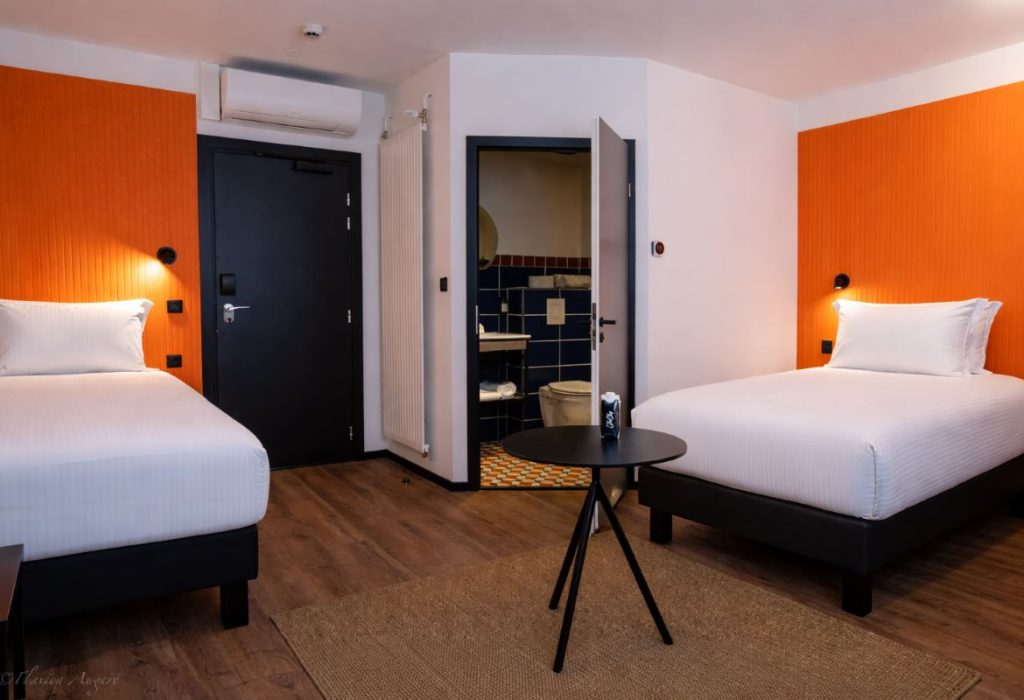 Chambre triple avec deux lits simples orange symétriques et salle de bain, séjour en famille Strasbourg