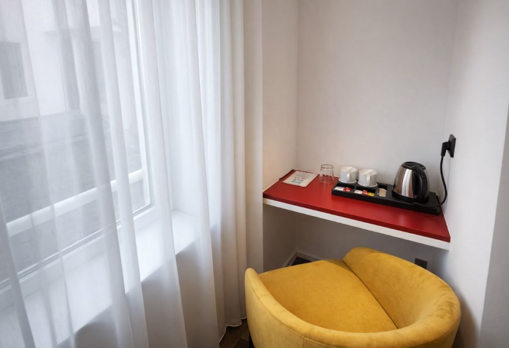 Coin bureau avec plateau rouge, bouilloire, tasses et fauteuil jaune près d'une fenêtre lumineuse
