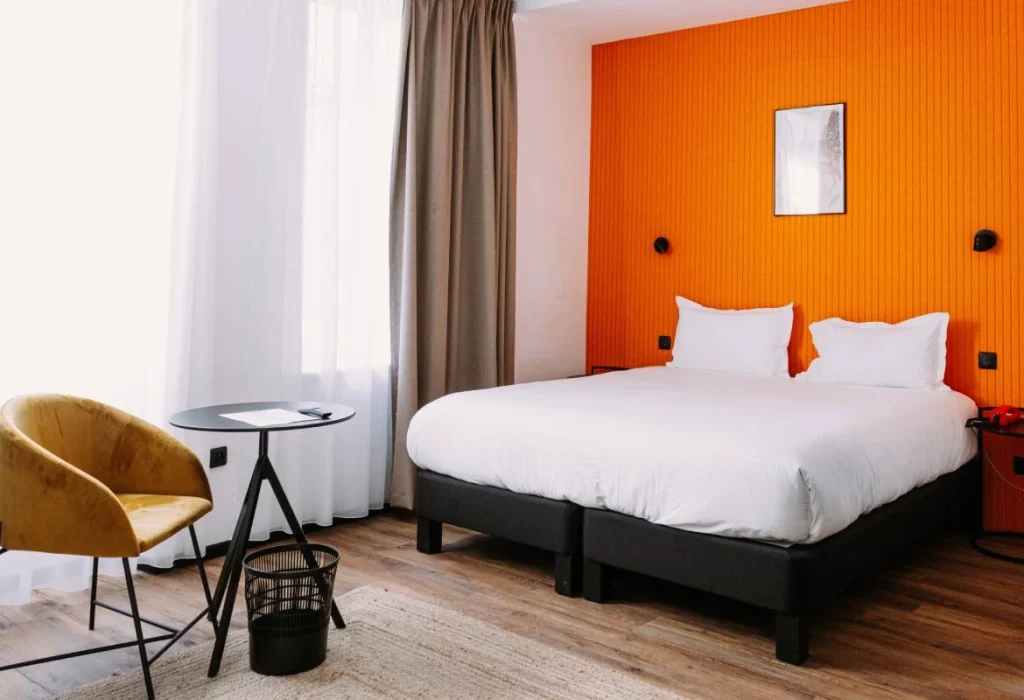 Chambre Quadruple du ClapClap Hôtel Strasbourg avec lit double, mur orange, fauteuil velours ocre et parquet