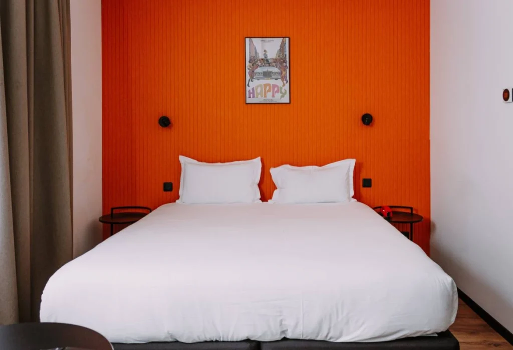Lit double de la chambre Quadruple du ClapClap Hôtel Strasbourg avec mur orange, affiche "Happy" et appliques noires