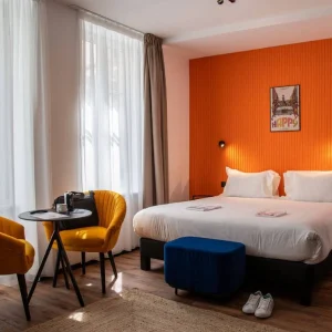 Chambre double avec mur orange et fauteuils jaunes à l'hôtel Clap Clap Strasbourg