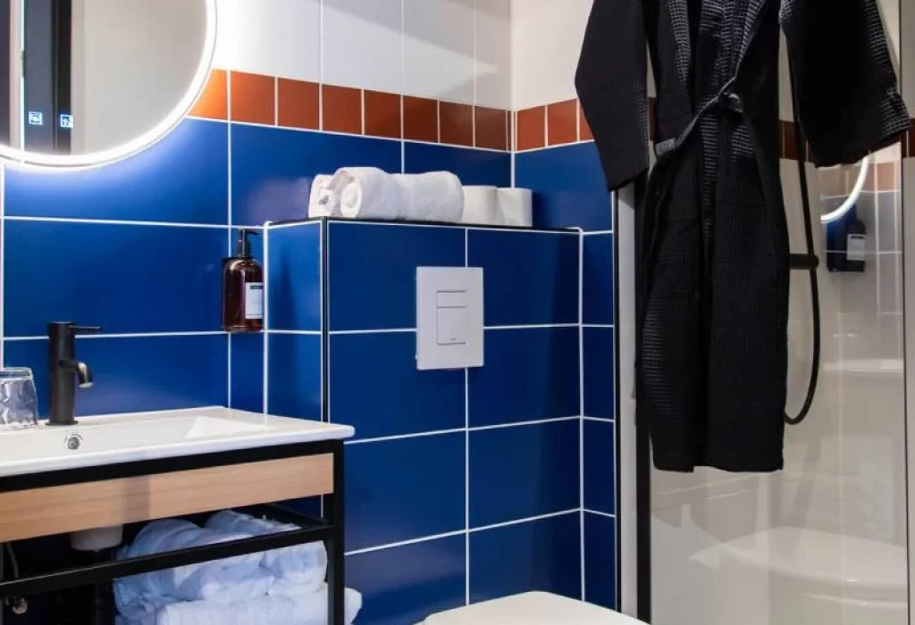 Salle de bain de la Chambre Star du ClapClap Hôtel Strasbourg avec carrelage bleu, miroir rétroéclairé, douche vitrée et peignoir