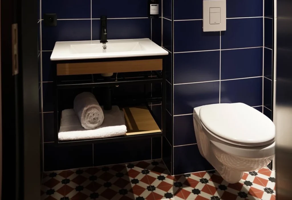 Salle de bain du ClapClap Hôtel Strasbourg avec vasque sur étagère bois, WC suspendu, carrelage bleu cobalt et sol carreaux de ciment