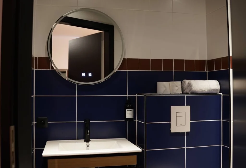 Salle de bain du ClapClap Hôtel Strasbourg avec vasque, robinetterie noire, miroir rond, carrelage bleu cobalt et frise bordeaux