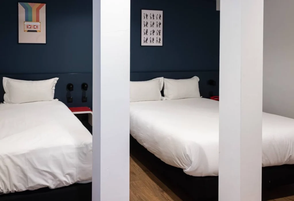 Deux lits côte à côte dans la chambre Tribu du ClapClap Hôtel Strasbourg avec mur bleu pétrole et affiches colorées
